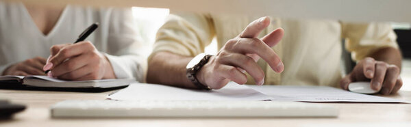 Cropped view of businessman pointing near intern writing on notebook in office, banner 