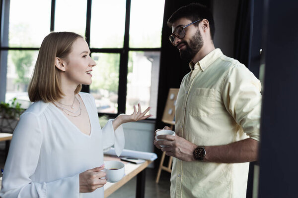 New worker with cup of coffee talking to manager in office 