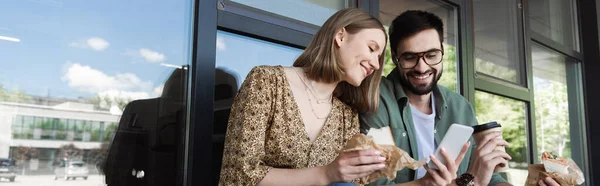 Kadını Elinde Sandviç Akıllı Telefon Ile Arkadaşının Yanında Kahve Binayla — Stok fotoğraf