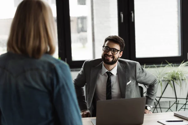 Smiling businessman in eyeglasses looking at blurred job seeker in office
