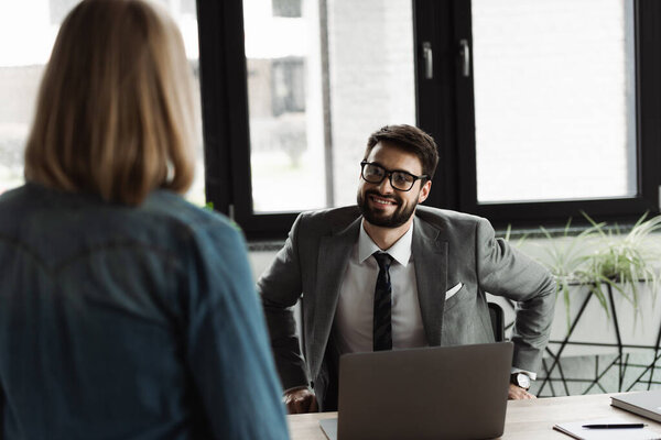 Smiling businessman in eyeglasses looking at blurred job seeker in office 