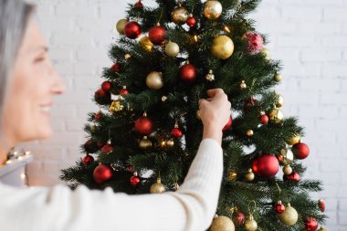 Bulanık ve neşeli orta yaşlı kadın. Gri saçlı, Noel ağacı süslemeli. 