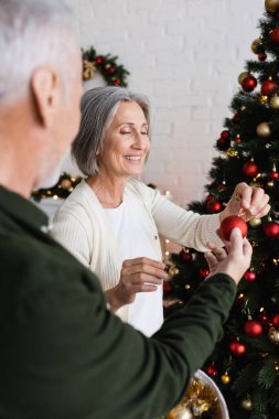 Olgun bir adam evinde çam ağacı süsleyen neşeli eşine Noel oyuncağı veriyor.