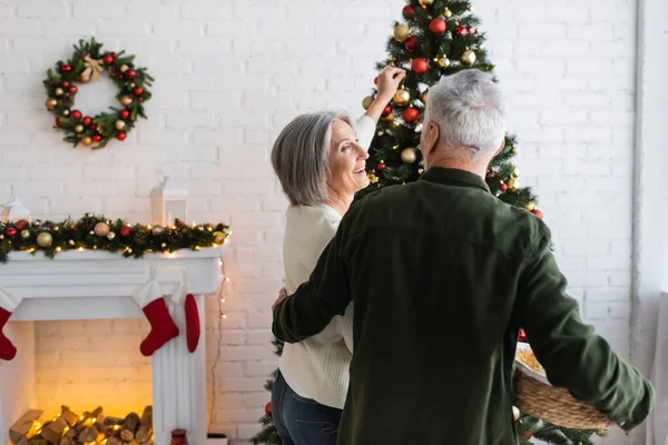 Smiling Middle Aged Woman Decorating Christmas Tree Looking Husband Holding — Stock Photo, Image