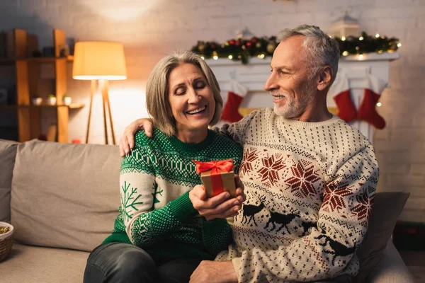 Happy Middle Aged Woman Holding Christmas Present Husband Sweater — Stock Photo, Image