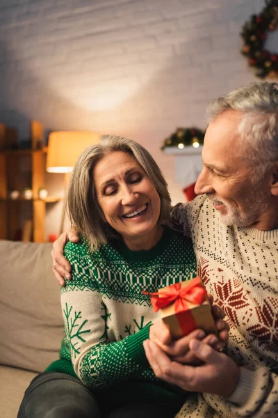 Cheerful Middle Aged Woman Holding Christmas Present Husband Sweater — Stock Photo, Image
