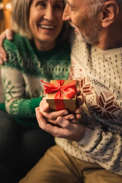 Happy Middle Aged Woman Holding Christmas Present Smiling Husband Sweater — Stock Photo, Image