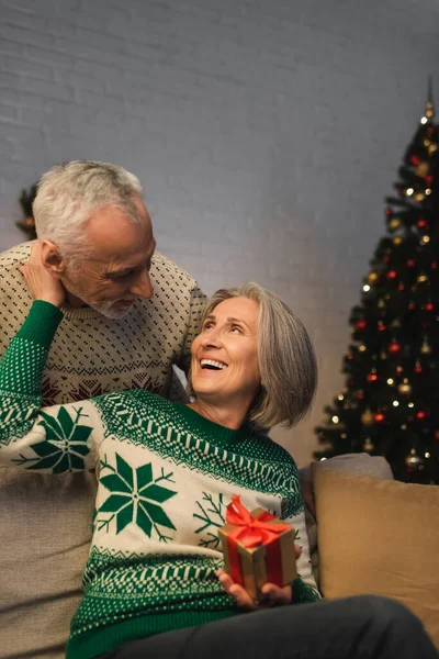 Feliz Mujer Mediana Edad Sosteniendo Regalo Navidad Abrazando Marido Suéter — Foto de Stock