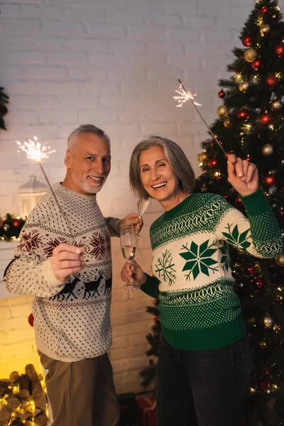 圣诞前夕 快乐的中年夫妇穿着节日毛衣 手里拿着火花和香槟酒 — 图库照片