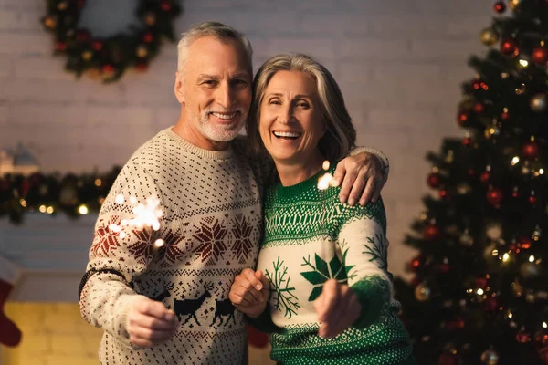 Happy Mature Couple Holiday Sweaters Holding Shiny Sparklers Christmas Eve — Stock Photo, Image