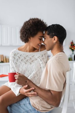 Beyaz kazaklı, baştan çıkarıcı Afro-Amerikan kadın mutfakta erkek arkadaşıyla yüz yüze oturuyor.