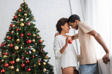 Mutlu Afrikalı Amerikalı kadın Noel balosuyla mutlu erkek arkadaşının yanında duruyor ve süslü ladin.