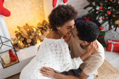 Beyaz kazaklı seksi Afro-Amerikalı kadın şöminenin yanındaki adama sarılıyor.