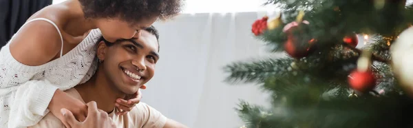 Young African American Woman Embracing Kissing Boyfriend Blurred Christmas Tree — Stock Photo, Image