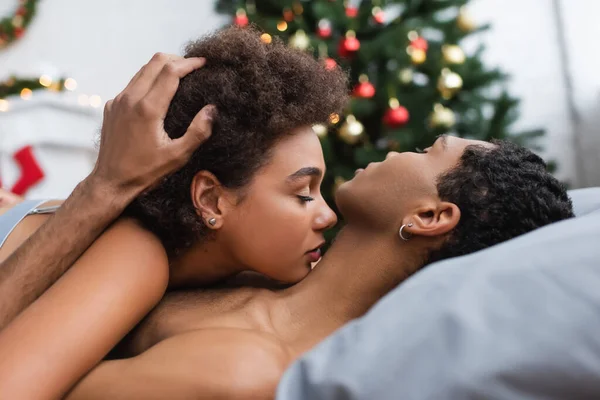 side view of african american man touching curly hair of sexy girlfriend on bed