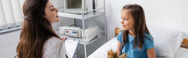 Elinde dosya olan gülümseyen doktor hastane koğuşundaki hastaya bakıyor. 