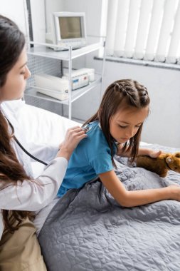 Steteskoplu çocuk doktoru hastane yatağında hastayı kontrol ediyor.  