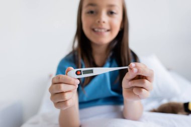 Blurred child holding electronic thermometer on bed in clinic  clipart
