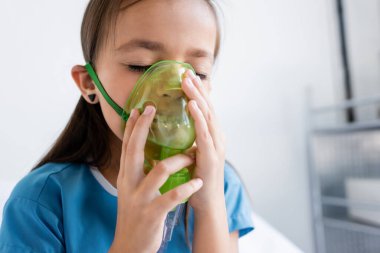 Klinikte oksijen maskesi takan hasta elbiseli bir çocuk. 