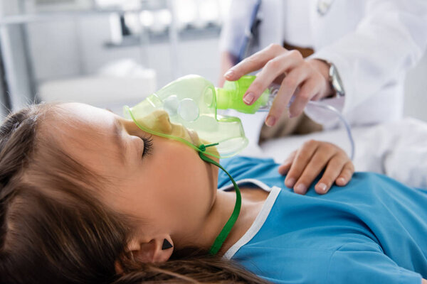Blurred pediatrician holding oxygen mask near sick child in hospital 
