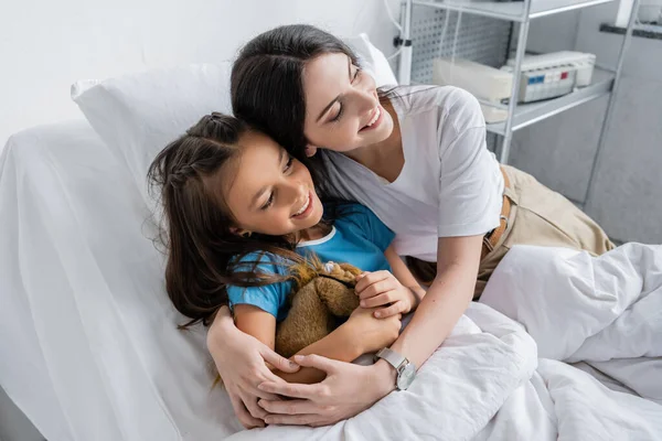 Klinikte Yatakta Oyuncak Taşıyan Mutlu Bir Ebeveyn Kızı Kucaklıyor — Stok fotoğraf