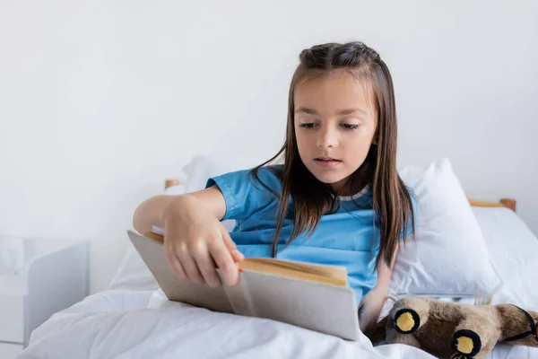 Gadis Berpakaian Pasien Membaca Buku Tempat Tidur Bangsal Rumah Sakit — Stok Foto