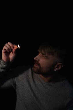 Elektrik kesintisi sırasında yanan kibritin ateşine bakan adam siyah ışıkta izole edilmiş.