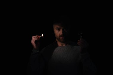 Ampullü ve kibritli bir adam siyah kameraya bakıyor.