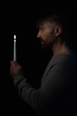 Siyah üzerine izole edilmiş karanlıkta yanan bir mum tutan yetişkin adam.