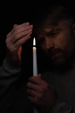 man holding hand near candle and looking at burning flame isolated on black clipart
