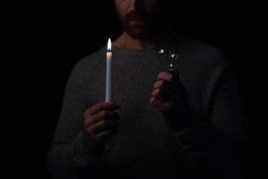 Enerji kesintisi sırasında elinde ampul ve mum tutan bir adamın görüntüsü siyahta izole edilmiş.