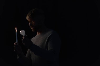 Elinde ampul ve yanan mum tutan adam karanlığa gömüldü.