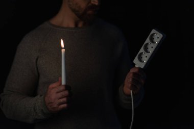 Elektrik kesintisi sırasında soketi uzatan ve mum yakan adamın kısmi görüntüsü siyahta izole edilmiş.