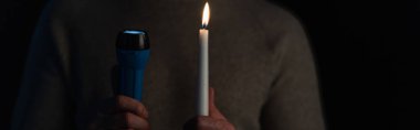 Elektrikli el feneri ve siyah pankartta izole edilmiş mum tutan adam görüntüsü.