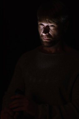 man lighting on face with flashlight while standing in darkness isolated on black clipart