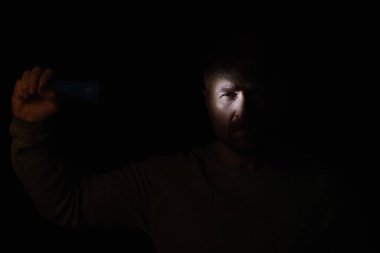 Karanlıktaki adam fenerle yüzünü aydınlatıyor ve siyah üzerine izole edilmiş kameraya bakıyor.