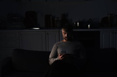 Adam enerji kesintisi sırasında karanlık mutfakta cep telefonuyla oturuyor.