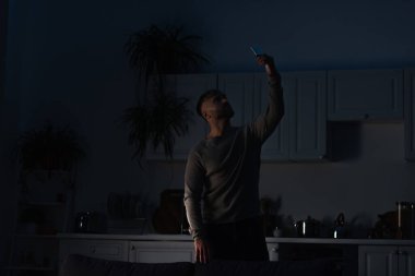 man holding smartphone in raised hand while searching for connection during energy blackout clipart