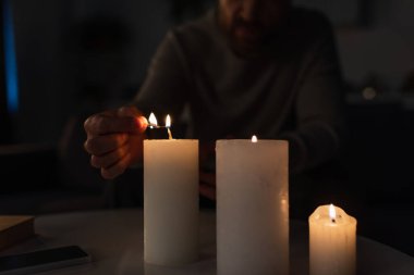 Elektrik kesintisi sırasında cep telefonunun yanında mum yakan adamın kısmi görüntüsü