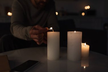 Karanlıkta mum yakan, akıllı telefonun yanında boş ekranlı kibrit yakan adam görüntüsü.