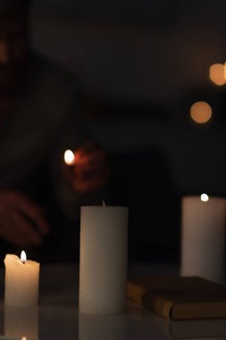 Bulanık arka planda, karanlıkta kırpılmış bir adamın yanında mum yakmanın seçici odağı