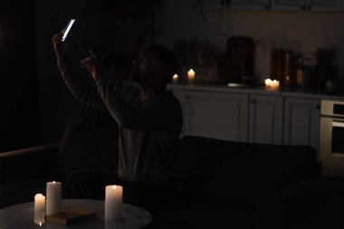 Adam karanlıkta yanan mumların yanında oturuyor ve akıllı telefondan cep telefonu bağlantısını yakalıyor.