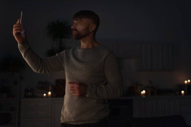 Cep telefonlu bir adam karanlıkta duruyor ve enerji kesintisi sırasında cep telefonu sinyali arıyor.