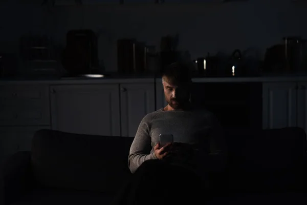 能源停电时坐在黑暗的厨房里拿着手机的男人 — 图库照片