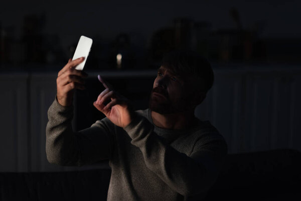 worried man pointing at cellphone while searching for mobile connection during electricity outage