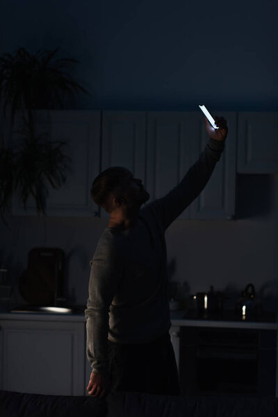 man searching for mobile connection while standing with smartphone in raised hand during power shutdown