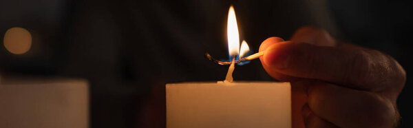 частичный вид человека зажигая свечу с горящей спичкой во время отключения электричества на черном фоне, баннер