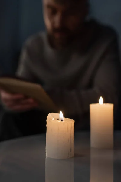 blurred man reading book in darkness near burning candles during energy blackout