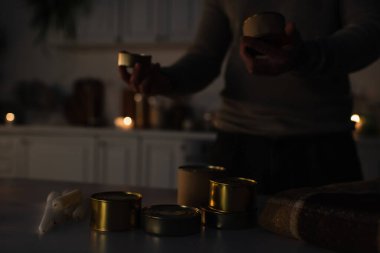 partial view of man near reserve of canned food and candles during power outage clipart