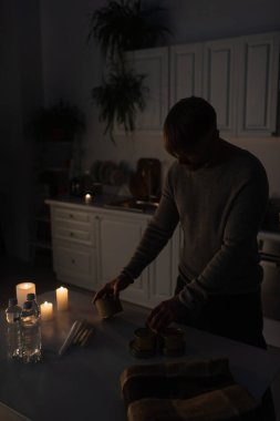 Elektrik kesintisi sırasında mutfakta konserve yiyecek ve mum tutan adam.